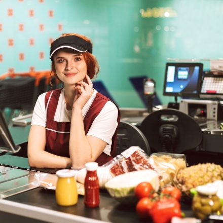 young-smiling-female-cashier-in-uniform-dreamily-Z74XGMA